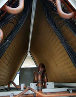 A close-up view of industrial equipment featuring a complex structure of metallic pipes and coils. Copper tubes are prominently visible, along with mechanical components and wiring neatly organized within a triangular frame.