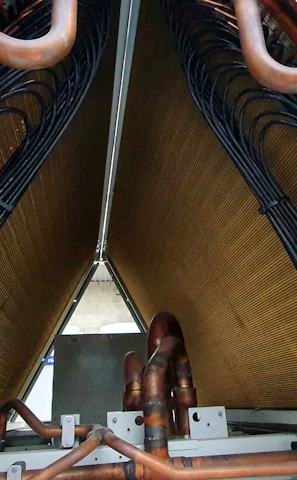 A close-up view of industrial equipment featuring a complex structure of metallic pipes and coils. Copper tubes are prominently visible, along with mechanical components and wiring neatly organized within a triangular frame.